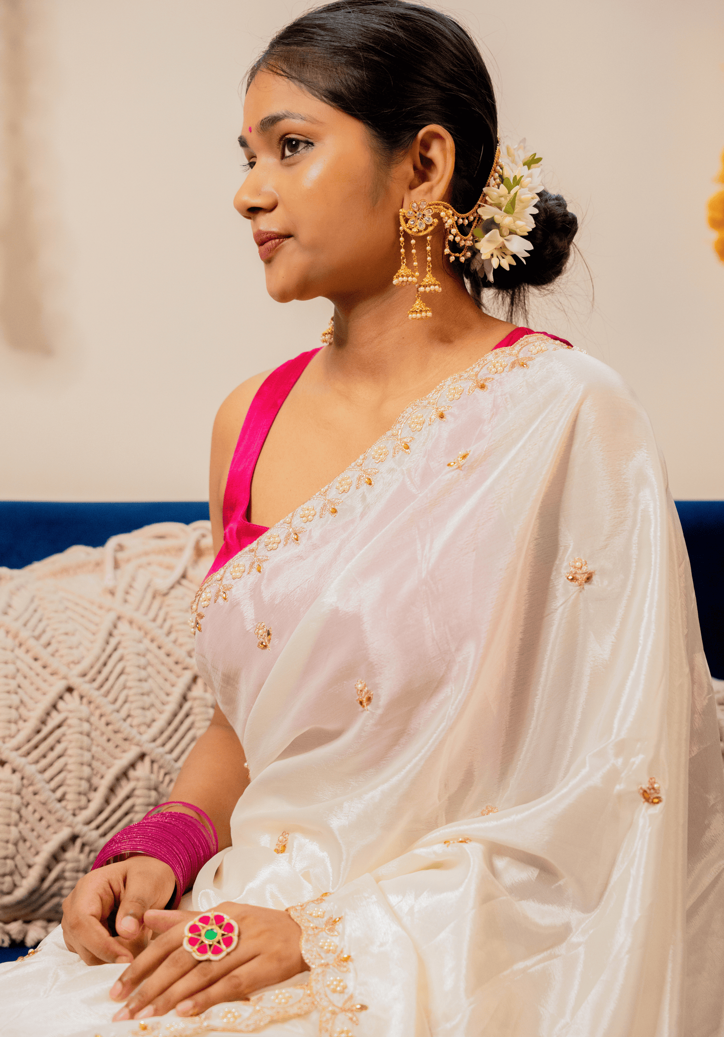 Woman wearing a white chinon saree with gold details and a pink blouse, sitting on a couch.