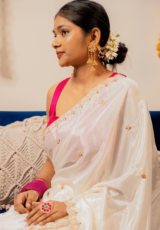 Woman wearing a white chinon saree with gold details and a pink blouse, sitting on a couch.