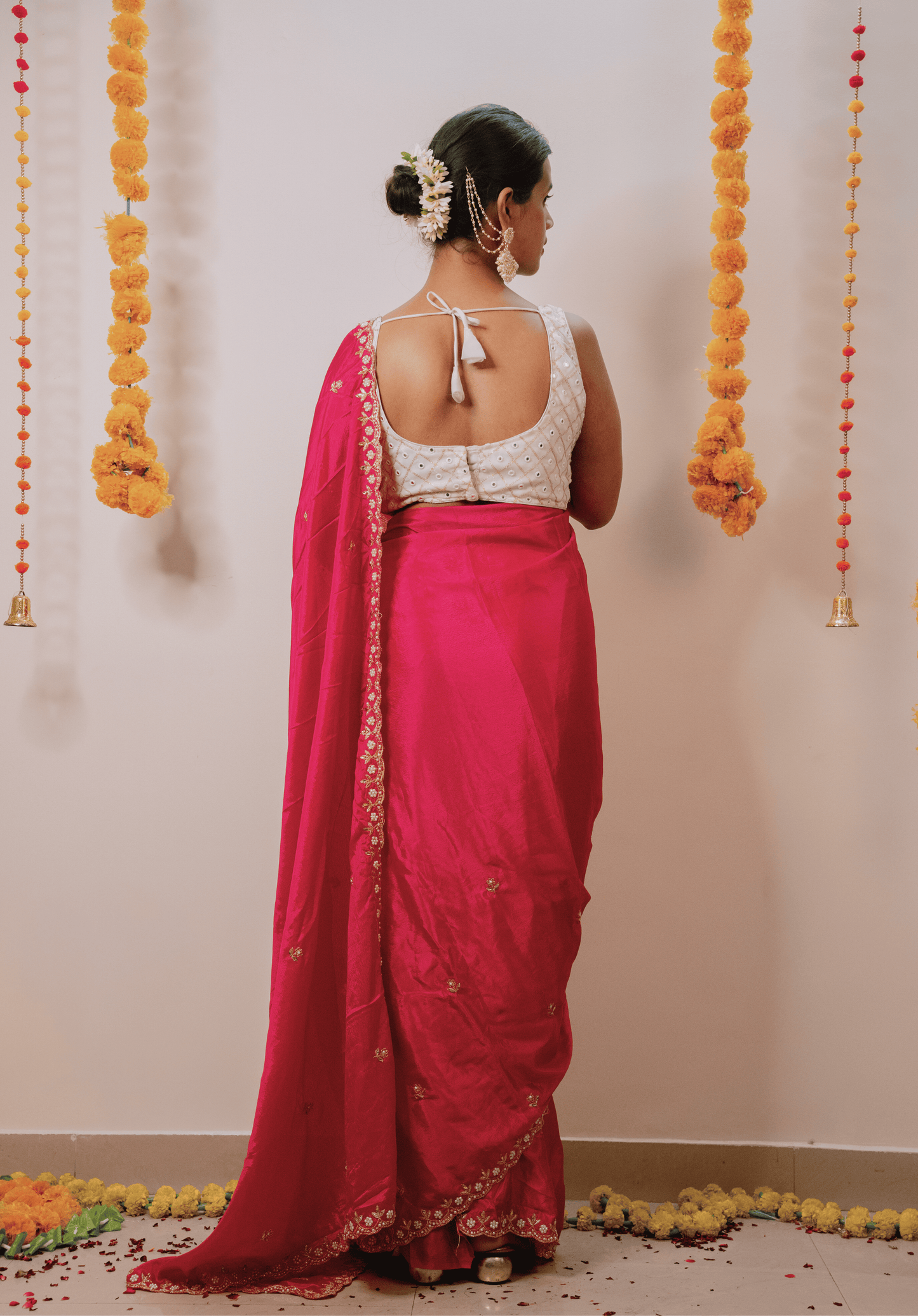 Woman in a pink chinon saree with a white blouse standing against a decorated wall.
