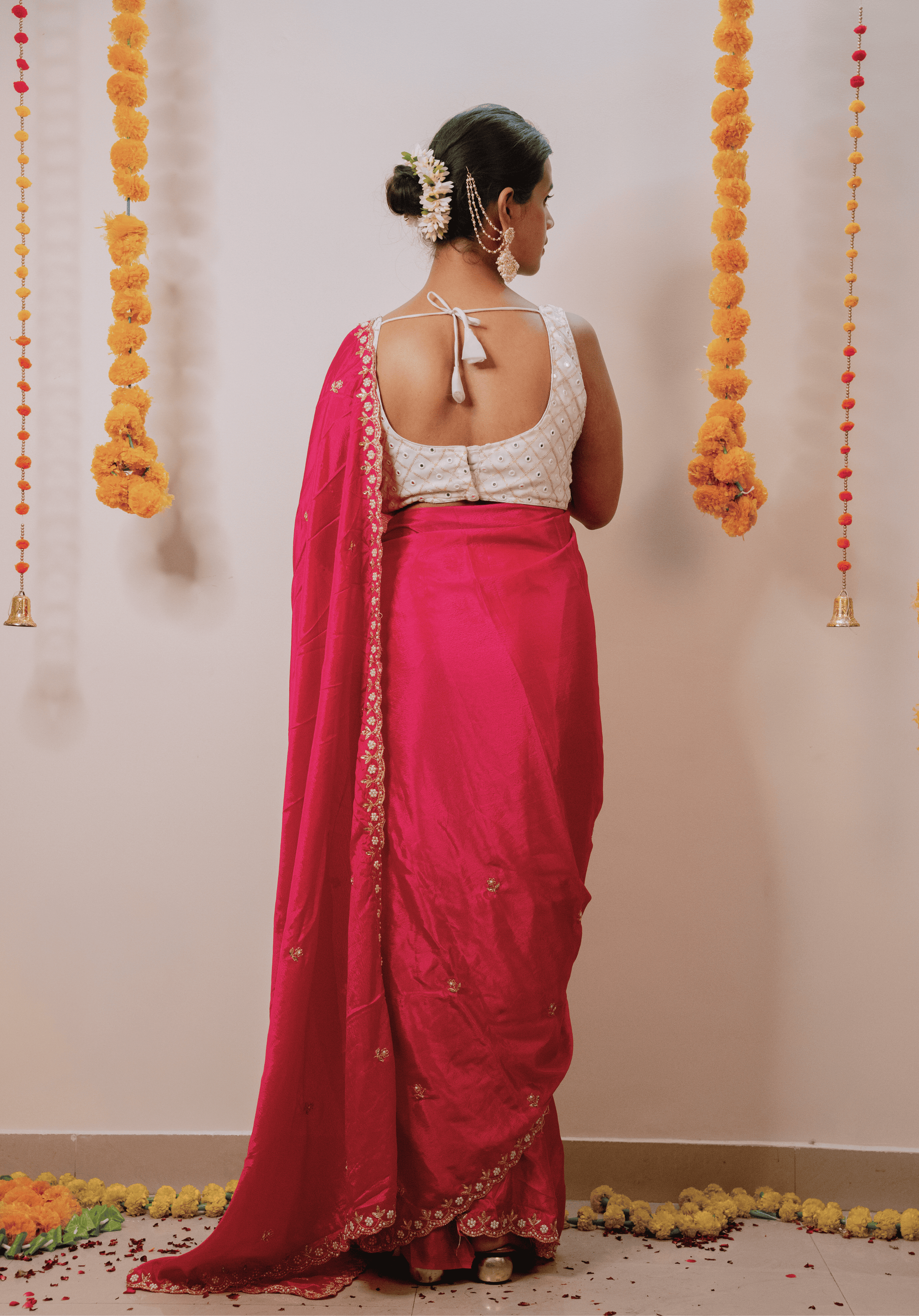 Woman in a pink chinon saree with a white blouse standing against a decorated wall.