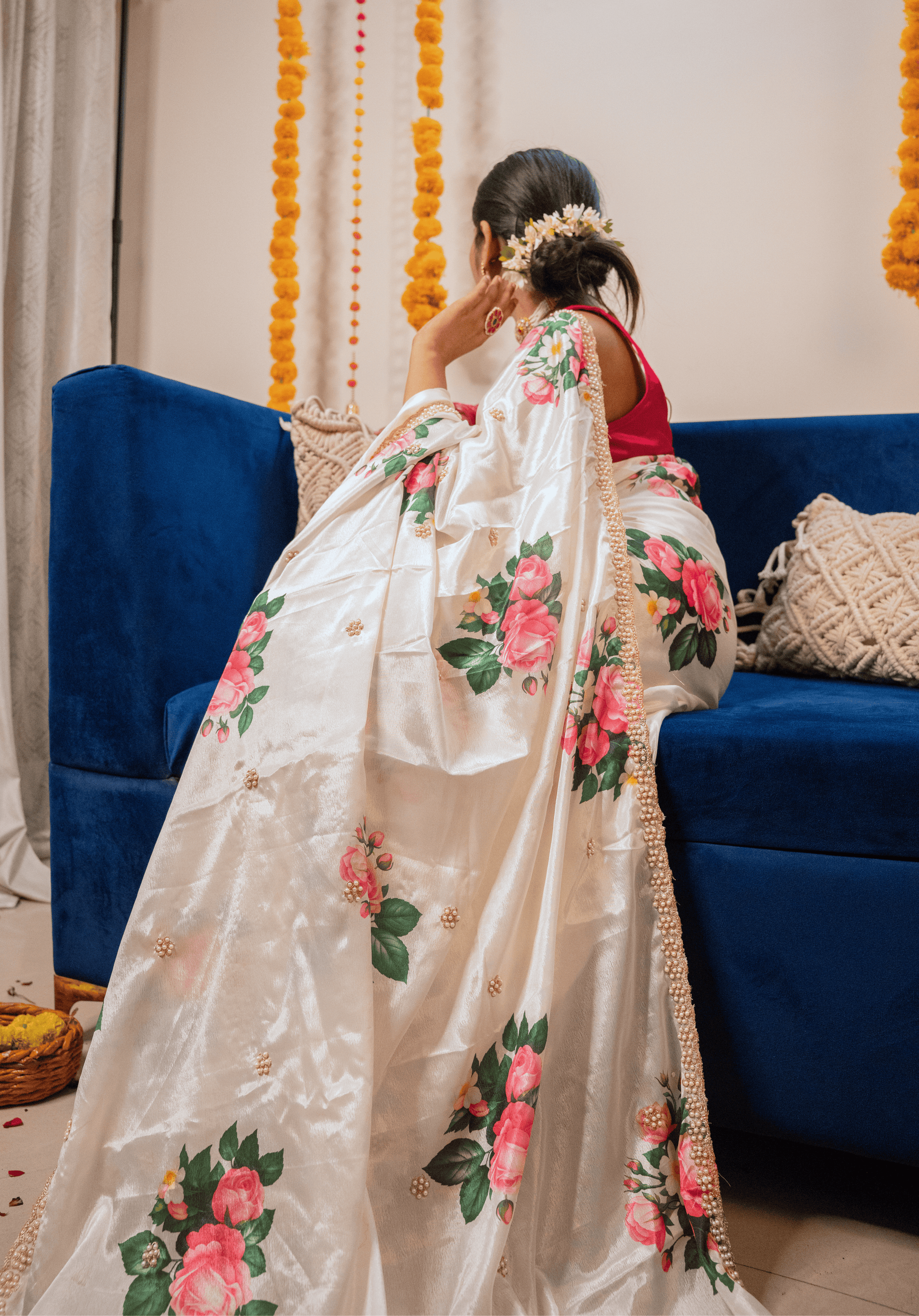 Woman in an ivory floral chinon saree sitting on a blue couch with decorative elements in the background.