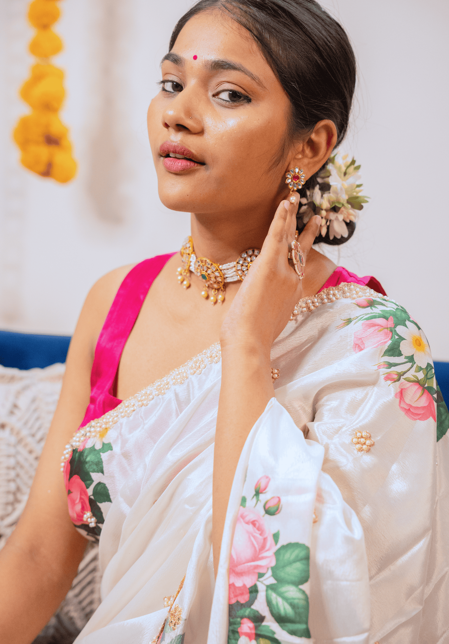 Woman in an ivory chinon saree with floral patterns and pink blouse, wearing gold jewelry.