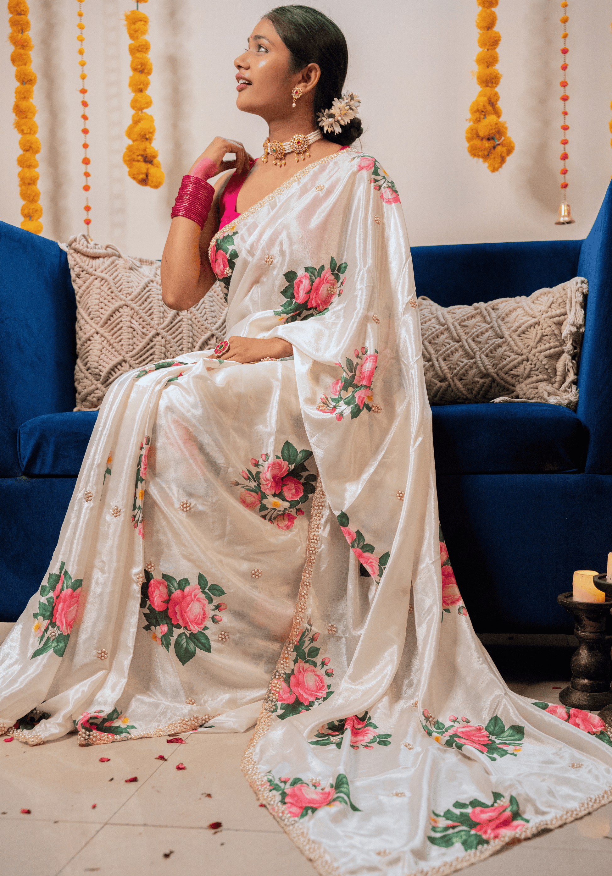 Woman in an ivory chinon saree with floral patterns sitting on a blue couch.