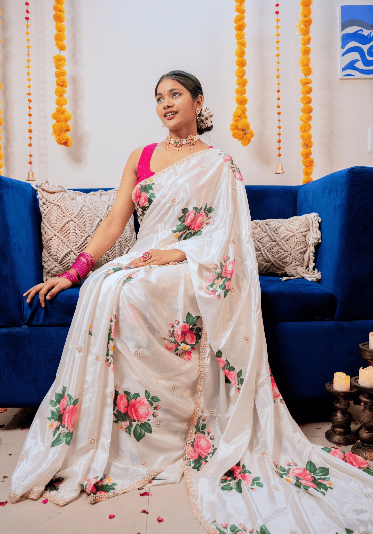 Woman in an ivory chinon saree sitting on a blue couch with decorative elements in the background