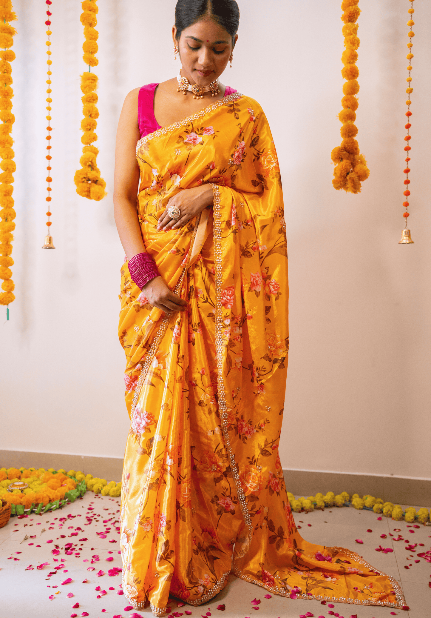 Woman in a mustard yellow floral embroidered chinon saree with pink blouse standing in a decorated room.