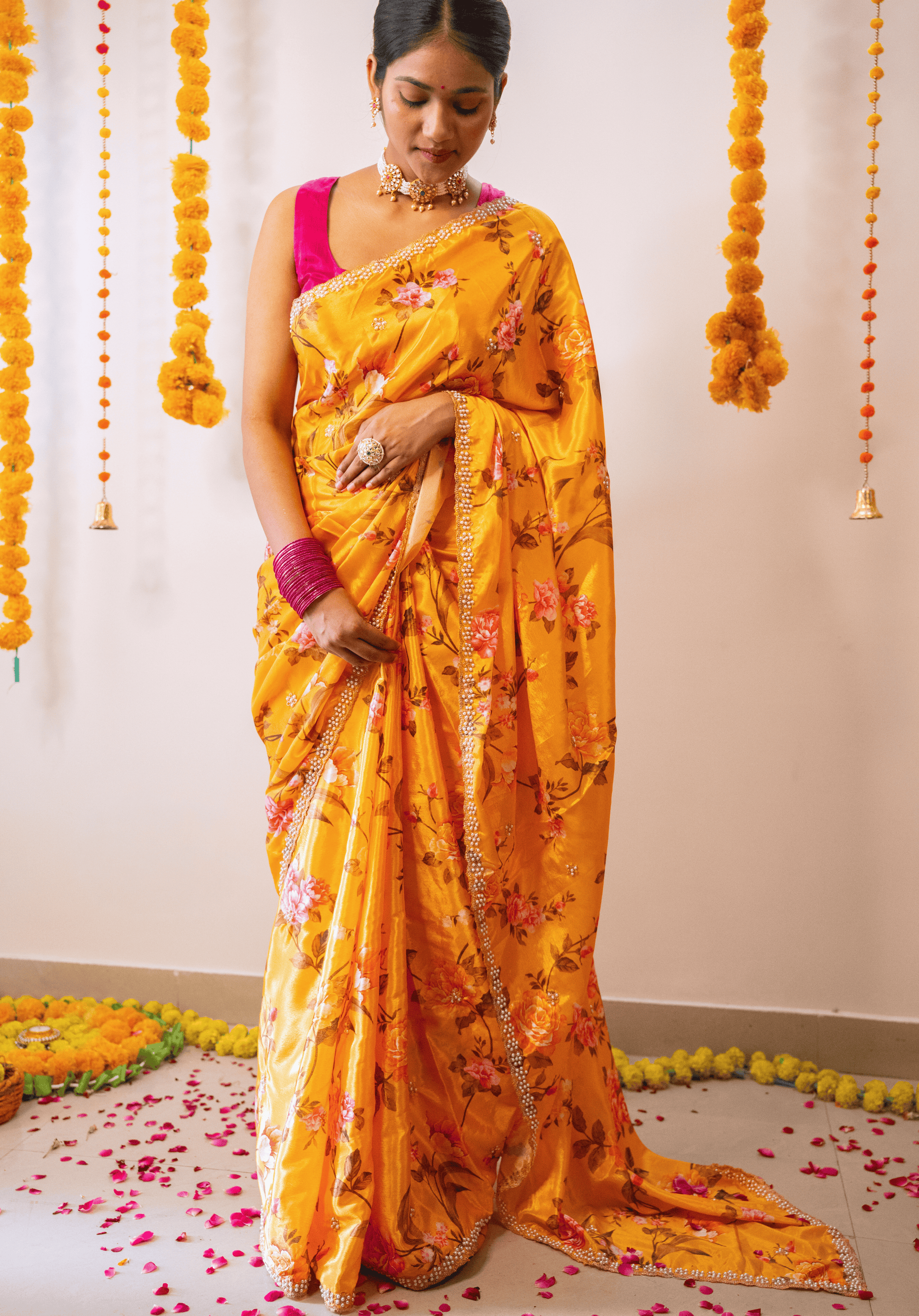 Woman in a mustard yellow floral embroidered chinon saree with pink blouse standing in a decorated room.