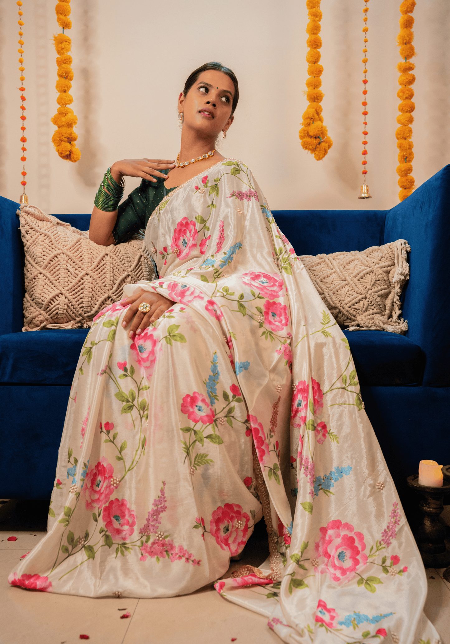Woman in an off white floral embroidered chinon saree sitting on a blue couch