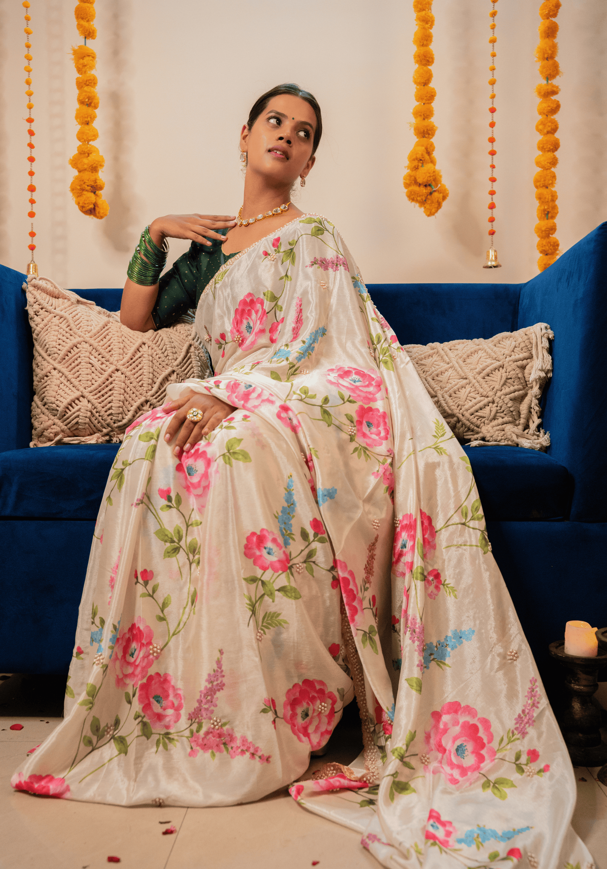 Woman in an off white floral embroidered chinon saree sitting on a blue couch