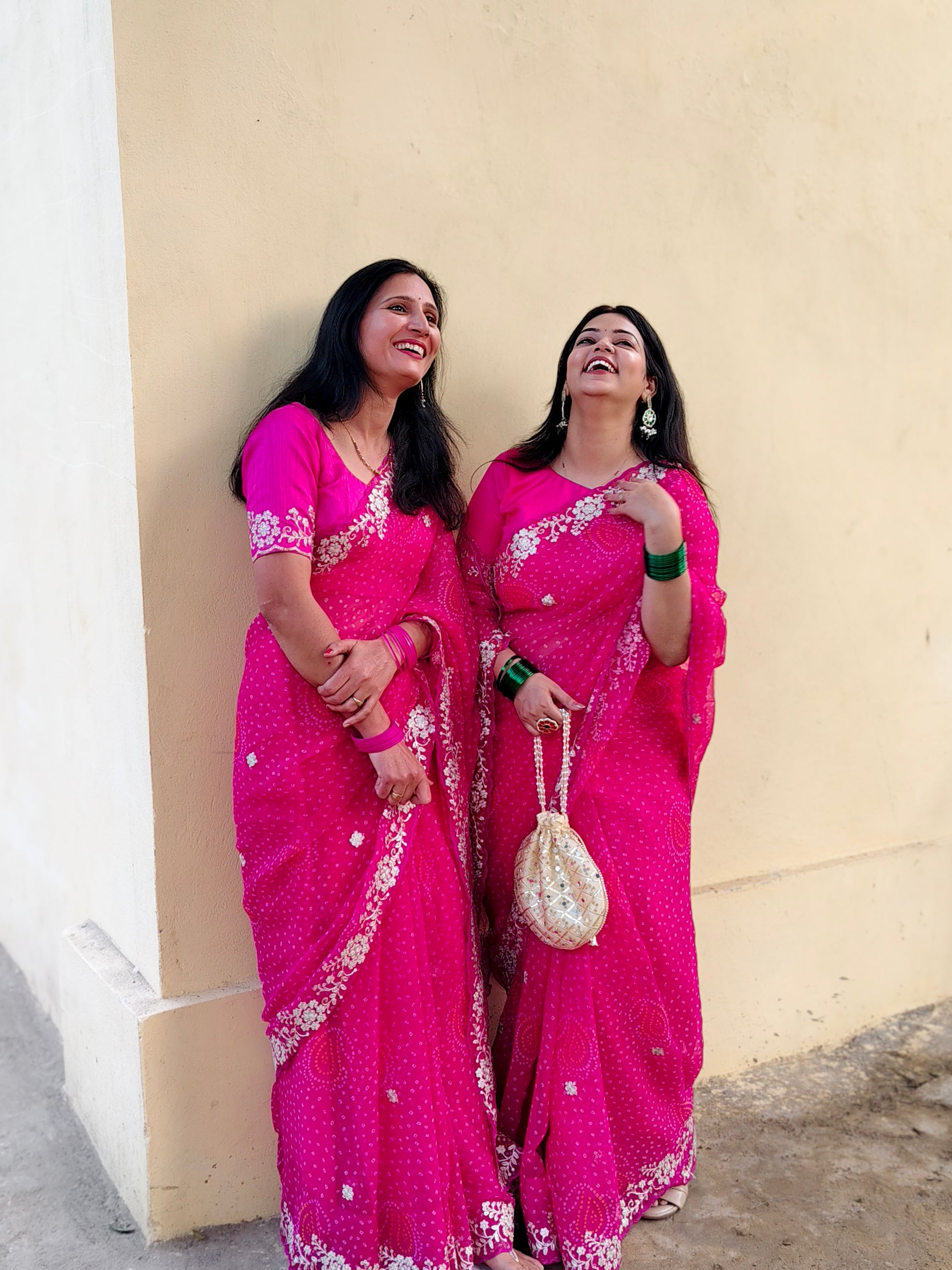 Two women in pink chiffon bandhani sarees.