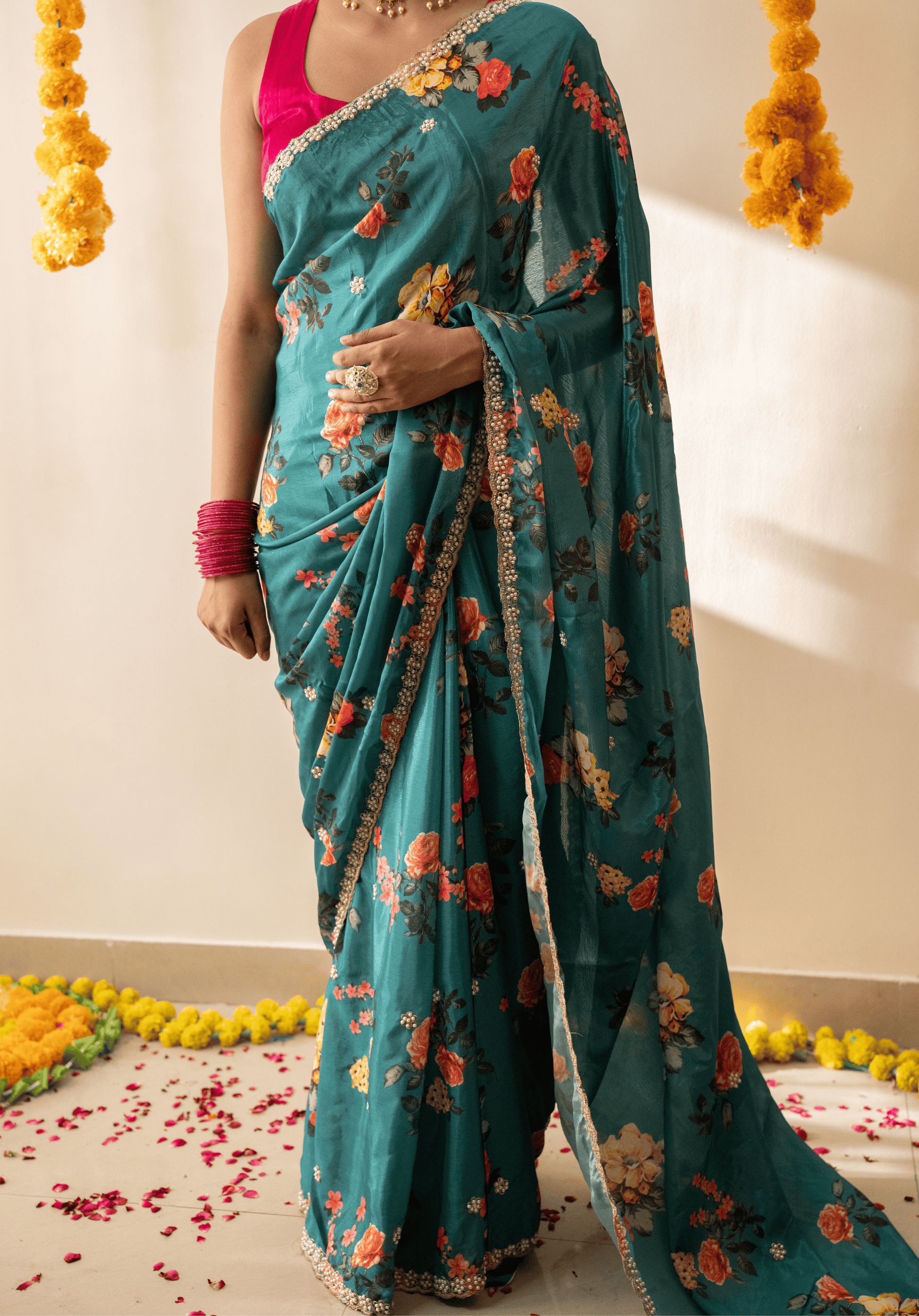 Woman wearing a teal green chinon saree with floral patterns and embroidered border.